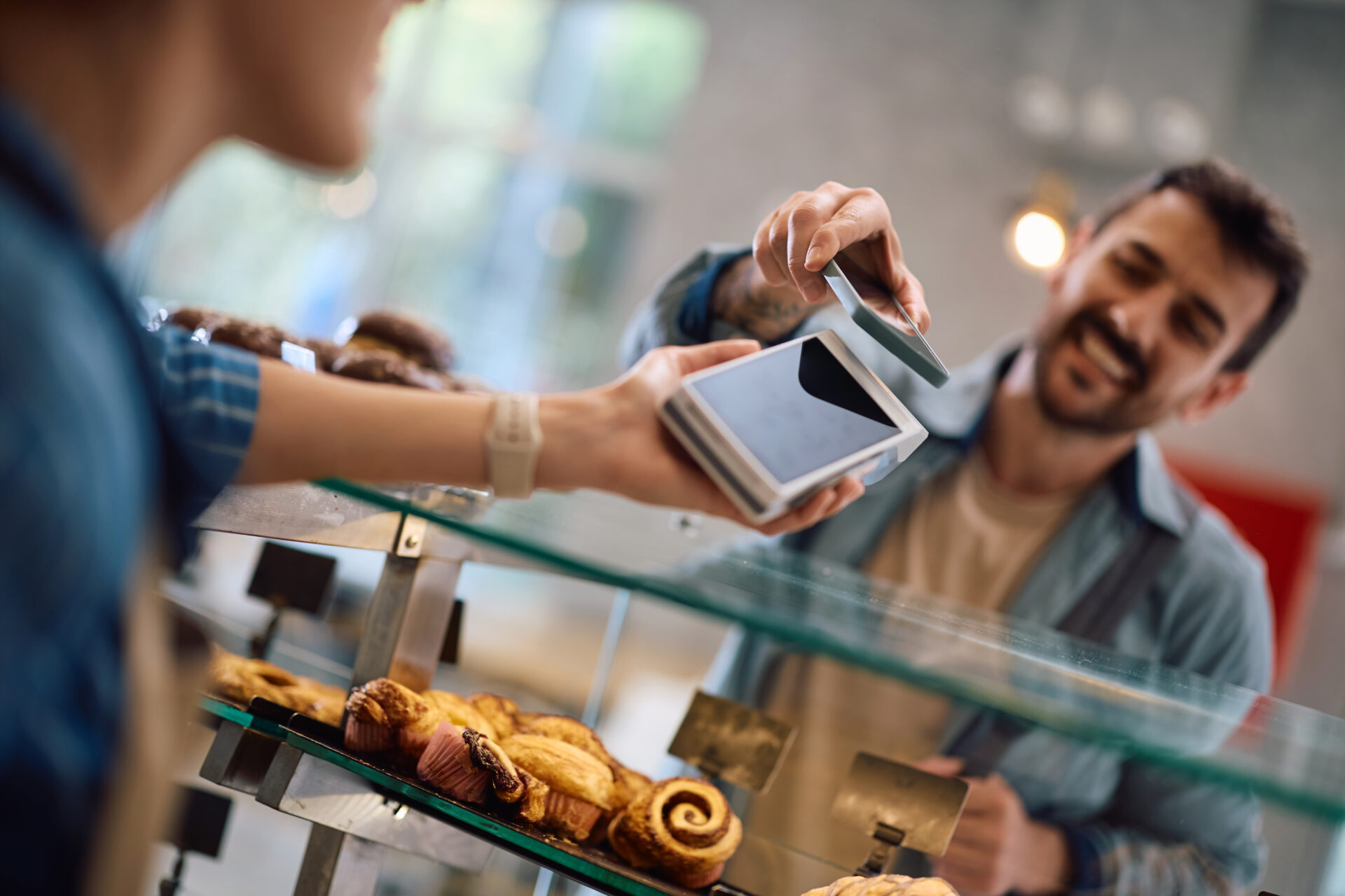 Close up of man using smart phone app while paying contactless in a bakery.