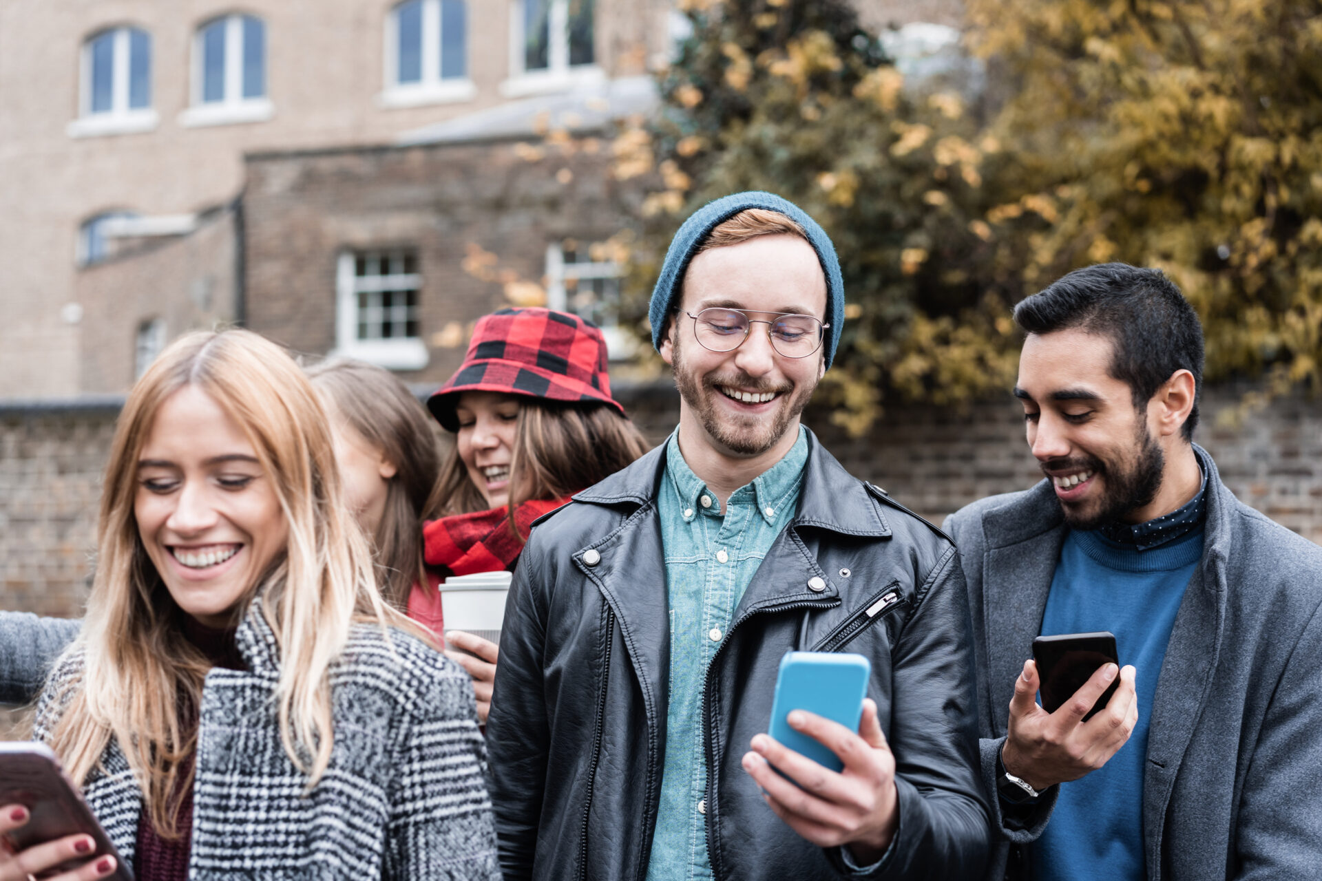 Young friends having fun using mobile phones outdoor in the city on winter day - Focus on center man face